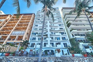 Ein mehrstöckiges Hotel mit Balkonen, Poolbereich und Palmen.