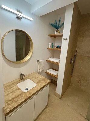 Ein Badezimmer mit rundem Spiegel, Waschbecken und Duschbereich.