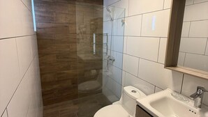 Moderni kylpyhuone, jossa on lasiseinällä varustettu suihku, wc ja pesuallas.