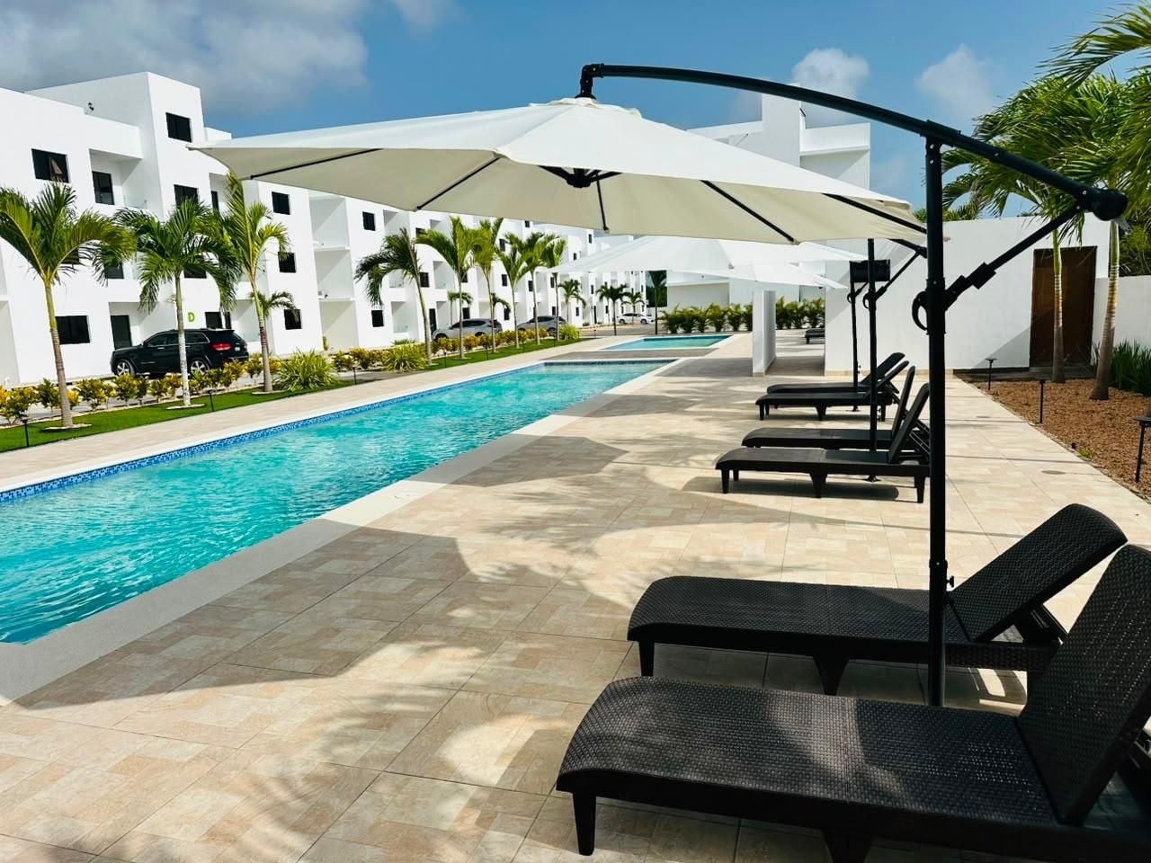 A swimming pool with lounge chairs and umbrellas, surrounded by a white building with balconies.