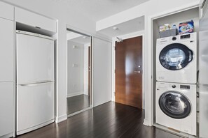 Une buanderie équipée d’un lave-linge et d’un sèche-linge à chargement frontal, d’une porte en bois et d’un mur blanc.