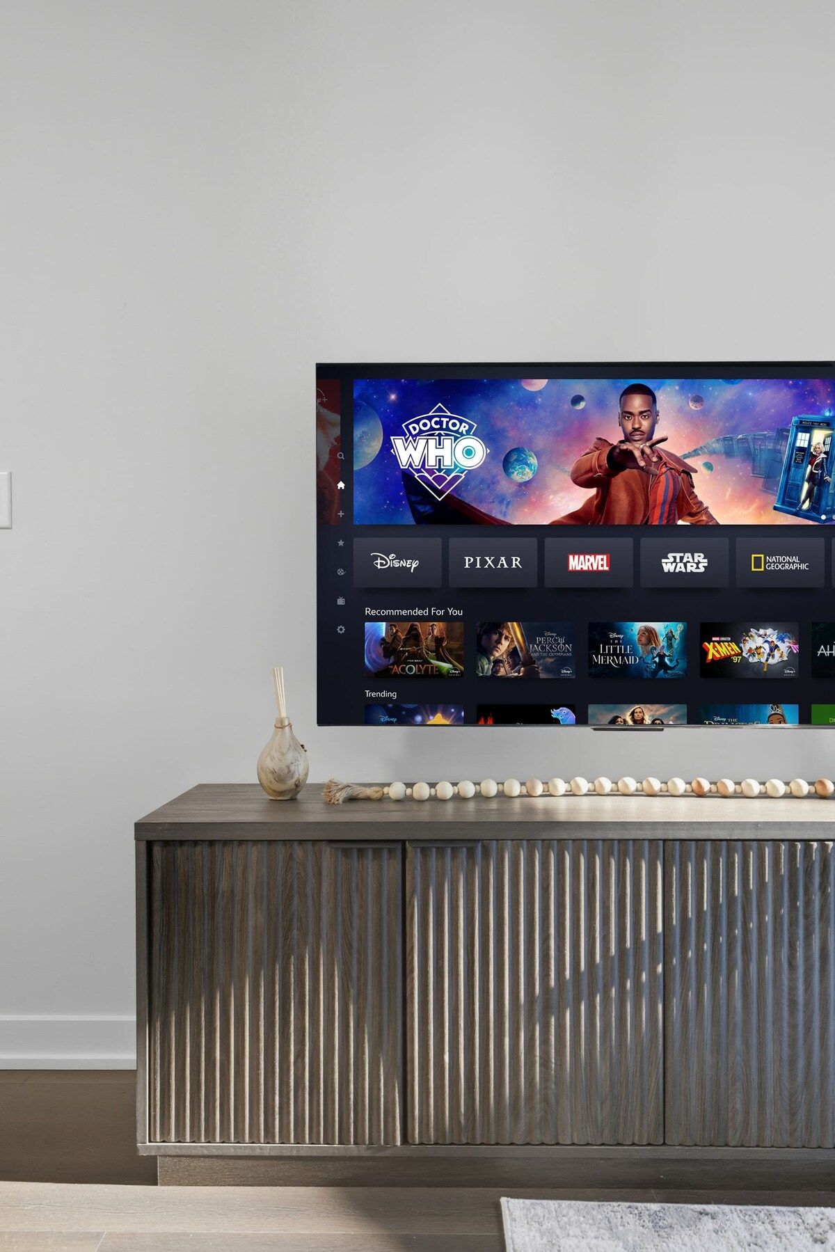 A flat-screen TV mounted on a wooden cabinet with a remote control on the right.