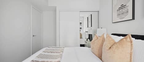 Una habitación de hotel con una cama, almohadas, una mesita de noche, una lámpara y una obra de arte enmarcada en la pared.