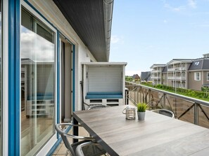 A balcony with a table and chairs, a potted plant, and a view of neighboring buildings. - Utholm 4a - Big Breeze (St. Peter-Ording)