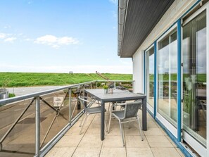 A balcony with a table and chairs, a railing, and a view of a green landscape. - Utholm 4a - Big Breeze (St. Peter-Ording)
