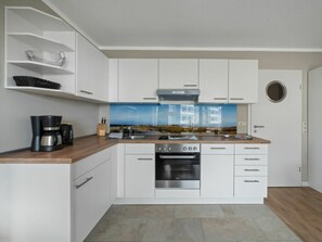 A modern kitchen with white cabinetry, a built-in oven, and a coffee maker on the counter. - Utholm 4a - Big Breeze (St. Peter-Ording)