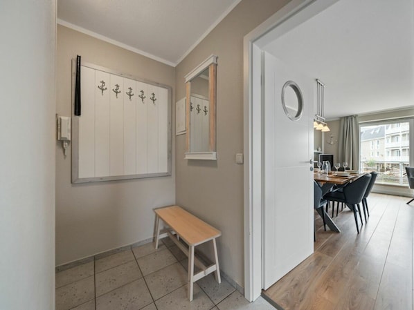 A hotel room with a wooden bench, a dining area with a table and chairs, and a large window offering a view of buildings. - Utholm 4a - Big Breeze (St. Peter-Ording)