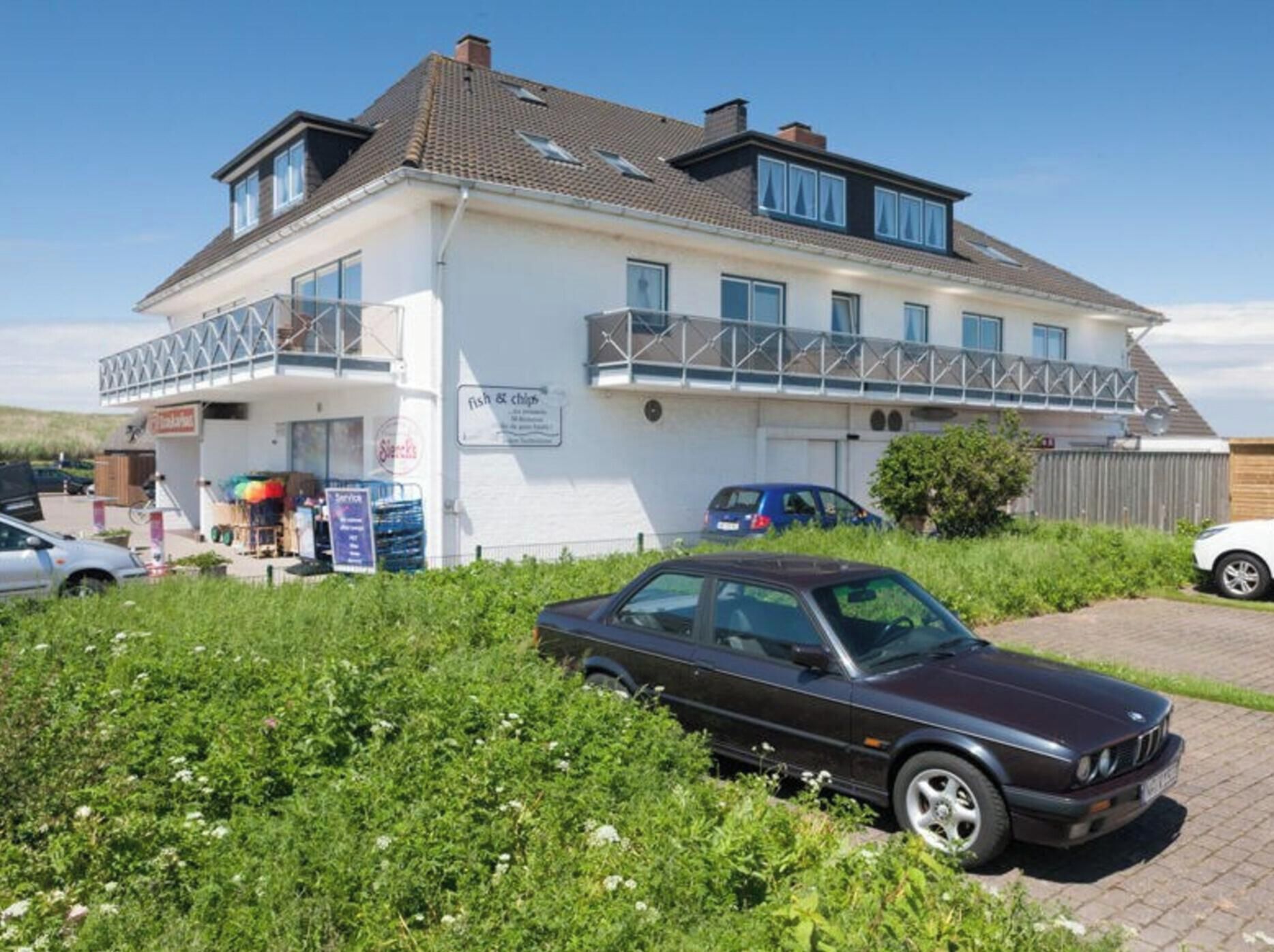A two-story building with a balcony, a sign for 'fish & chips', and a parked car in the foreground.