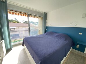 Ein Schlafzimmer mit einem Bett, einem Fenster mit Vorhängen und Blick auf Gebäude.