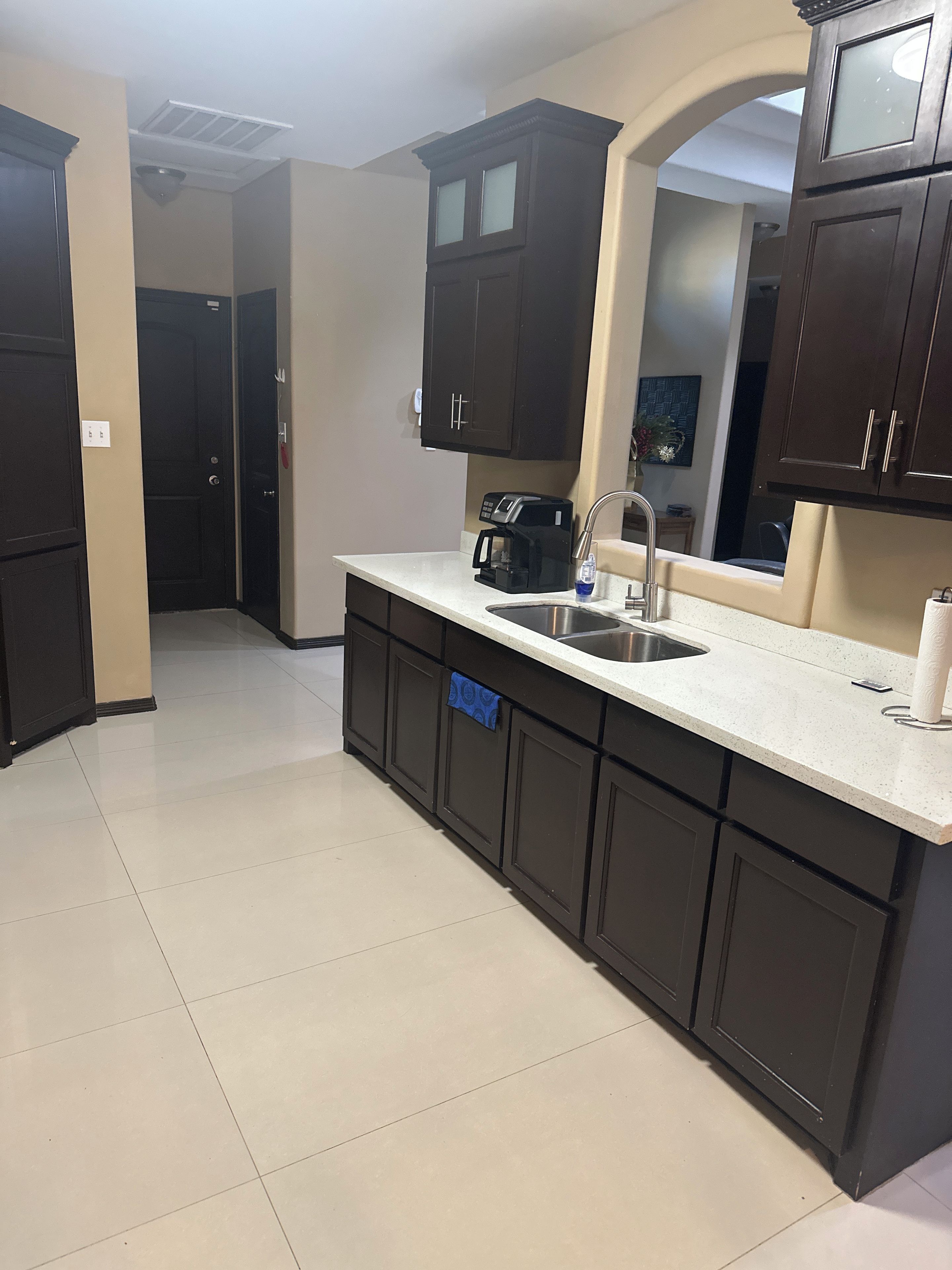 A kitchen with dark cabinets, a white countertop, a coffee maker, and a sink.