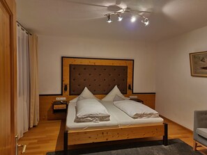Ein Schlafzimmer mit einem hölzernen Bett, einem Nachttisch, einer Wandheizung und einem grauen Sessel.