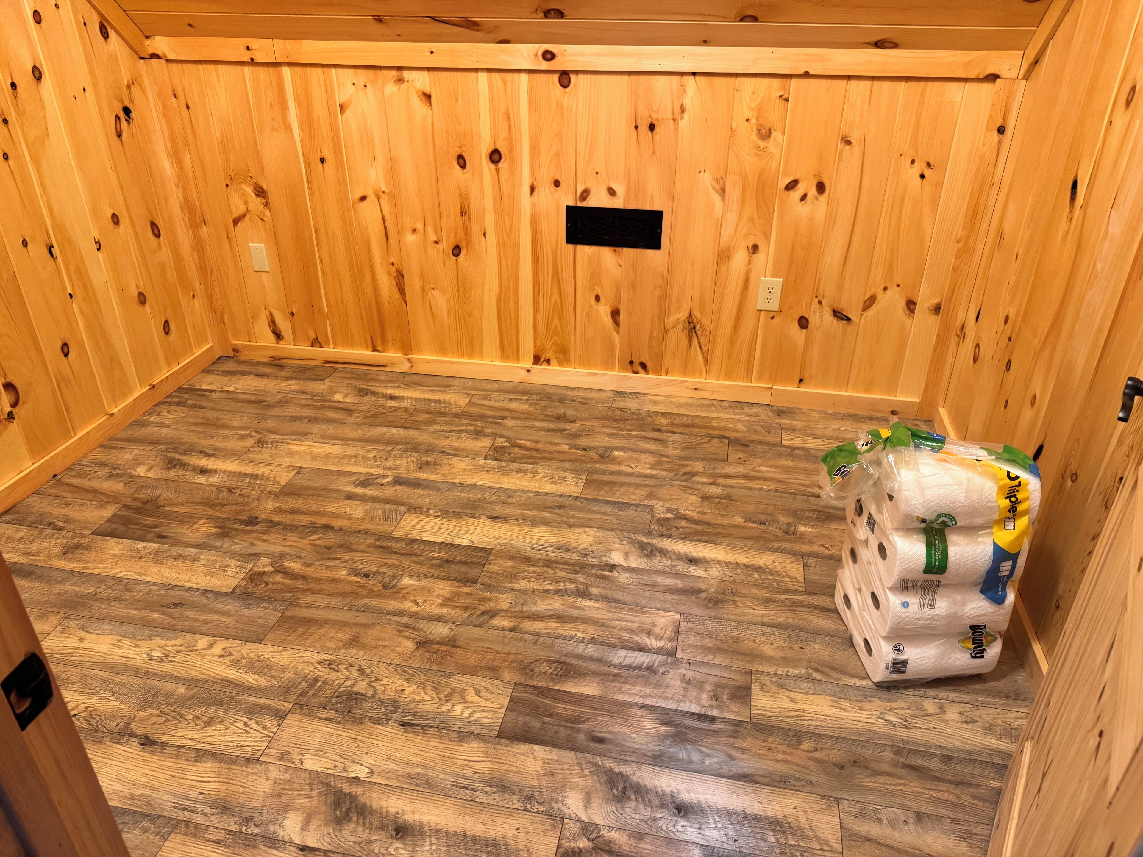 Une pièce aux murs en bois et au plancher orné d’un motif en chevrons. Un tas d’essuie-tout est posé sur le sol.