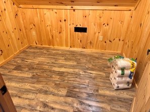A room with wooden walls and a herringbone-patterned floor. There is a stack of paper towels on the floor.