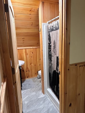 A wooden interior with a white sink, a toilet, and a shower area with a window.