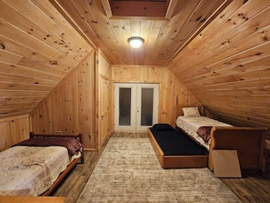 A small, wooden room with two beds, a single bench, and a door with a window.