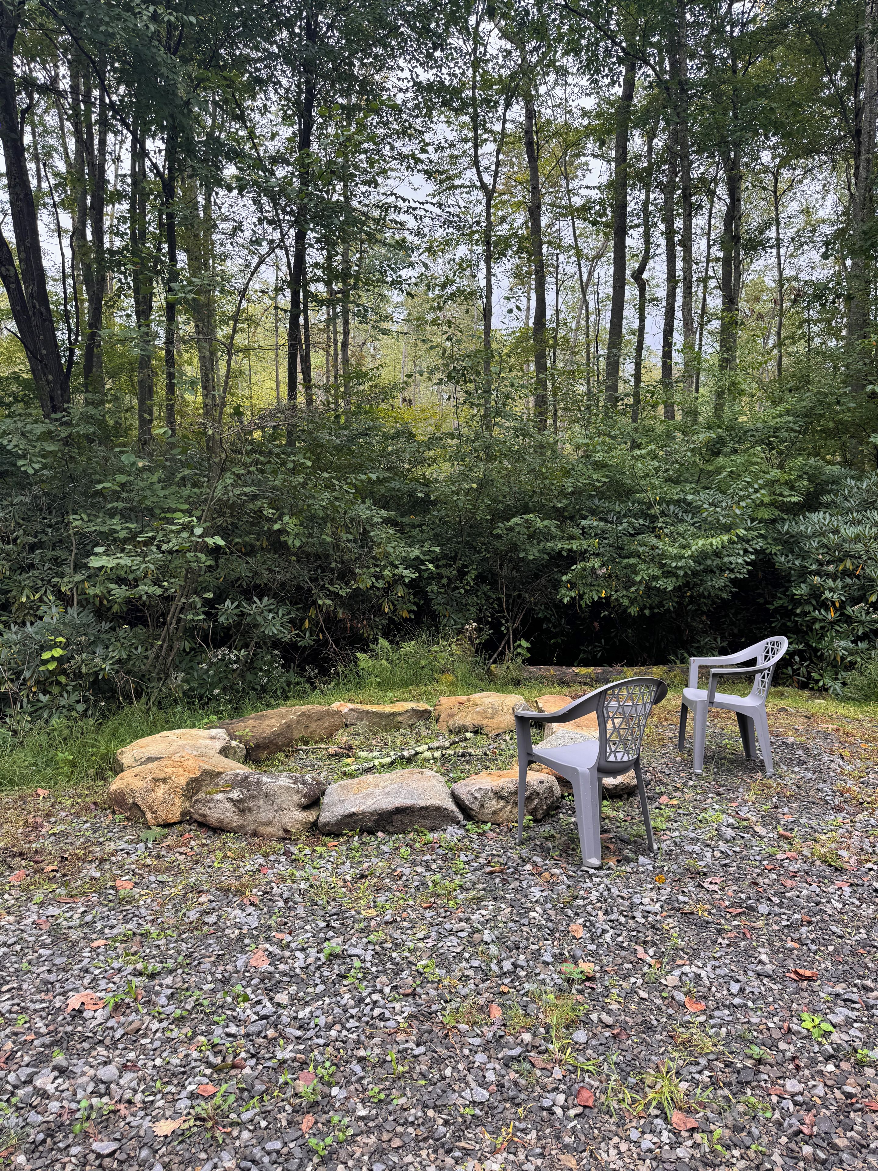 A natural outdoor setting with a seating area consisting of two chairs and a table, surrounded by rocks and vegetation.
