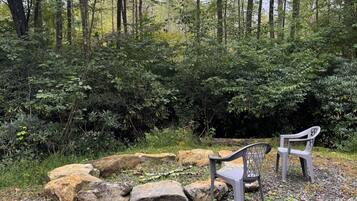 A natural outdoor setting with a seating area consisting of two chairs and a table, surrounded by rocks and vegetation.