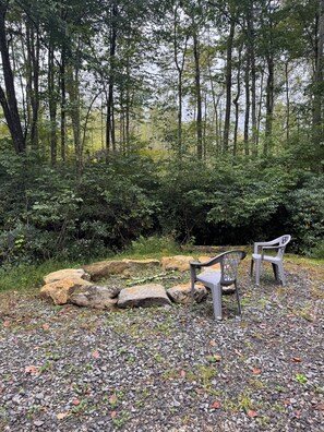 Entorno natural al aire libre con una zona de estar que incluye dos sillas y una mesa, rodeada de rocas y vegetación.