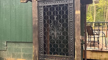 Una struttura in legno con un cancello in metallo decorativo, un piccolo portico con una sedia e un edificio verde sullo sfondo.