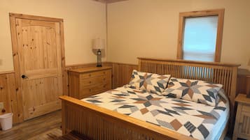 Un dormitorio con cama de madera, mesita de noche, cómoda, ventana y puerta.