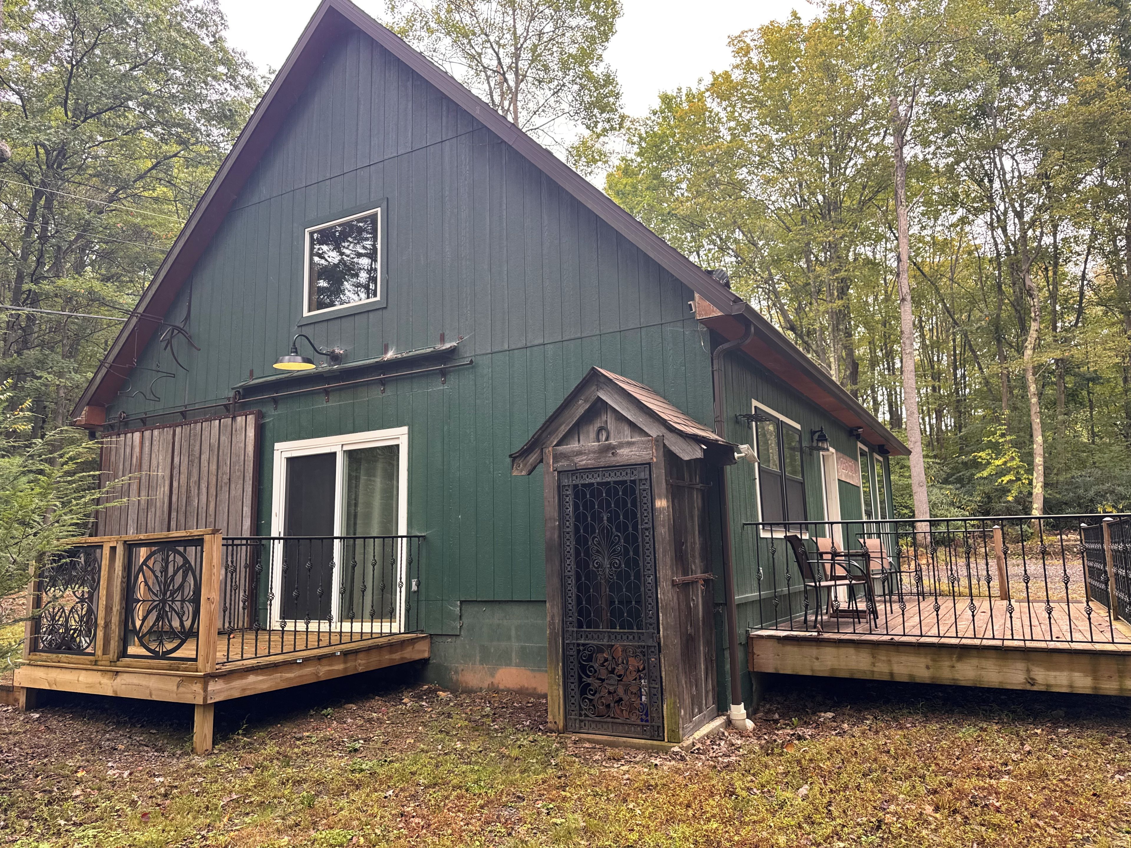 A two-story cabin with a deck, a front door with a decorative metal gate, and a large window above the door.