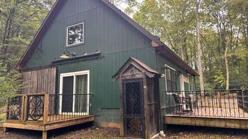 A two-story cabin with a deck, a front door with a decorative metal gate, and a large window above the door.