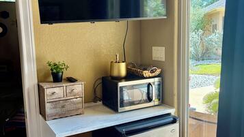 A compact kitchenette with a microwave, a small refrigerator, a television mounted above the counter, and a potted plant on the counter.