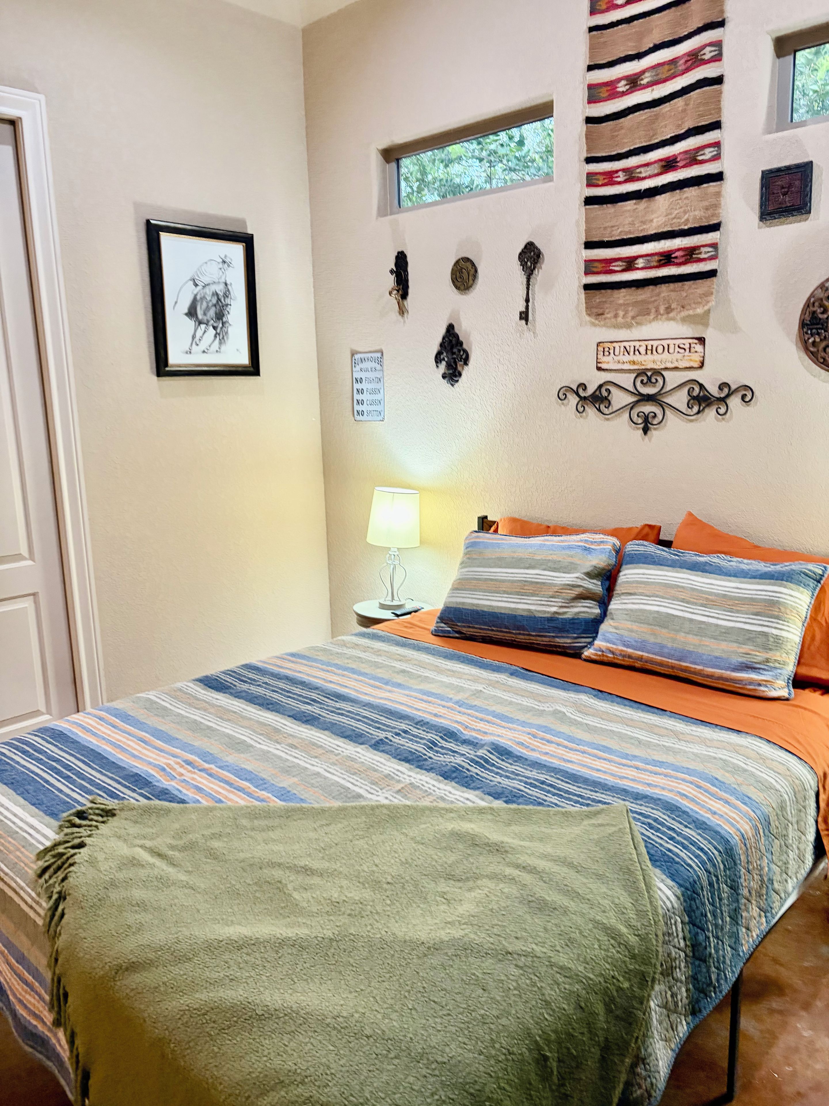 A bedroom with a bed, pillows, a nightstand, a lamp, and wall decorations including a sign and a tapestry.