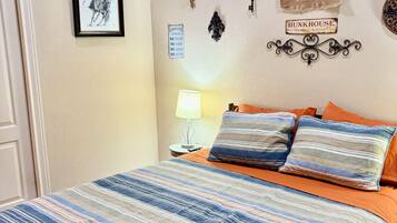 A bedroom with a bed, pillows, a nightstand, a lamp, and wall decorations including a sign and a tapestry.