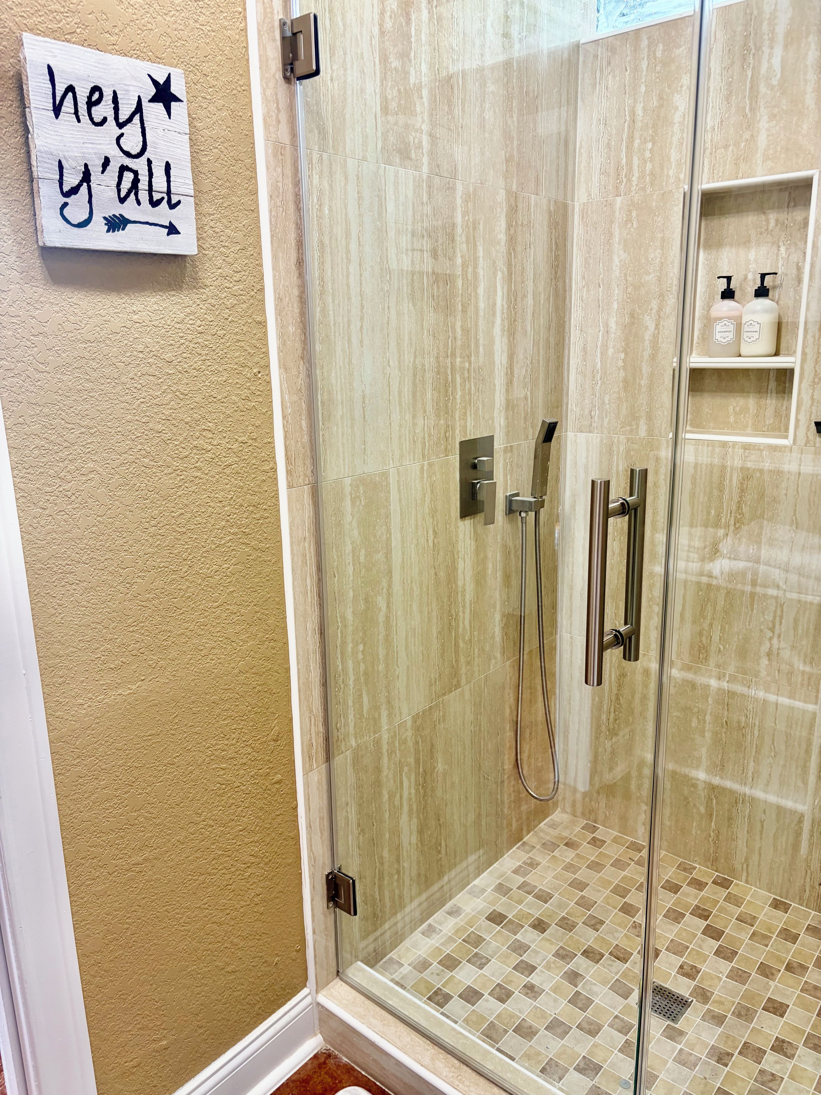 A glass-enclosed shower with a tiled floor, a hand shower, and a handheld showerhead.
