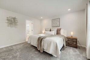 A bedroom with a bed, bedside lamps, a wooden nightstand, and a wall art piece. -     Stylish 4BR Home, Fenced Yard, Office + Tesla Charger (Dallas)