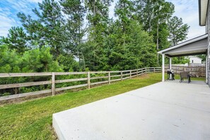 A covered patio area with a concrete floor, a wooden fence, and a view of a backyard with trees and a house. -     Stylish 4BR Home, Fenced Yard, Office + Tesla Charger (Dallas)