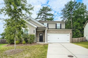 A two-story house with a garage, a brick facade, and a front yard with a tree and shrubs. -     Stylish 4BR Home, Fenced Yard, Office + Tesla Charger (Dallas)