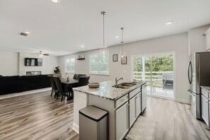 A modern kitchen with a central island, built-in appliances, and a dining area with a black sofa and chairs. -     Stylish 4BR Home, Fenced Yard, Office + Tesla Charger (Dallas)