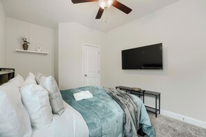 A bedroom with a bed, a television, a ceiling fan, and a door. -     Stylish 4BR Home, Fenced Yard, Office + Tesla Charger (Dallas)
