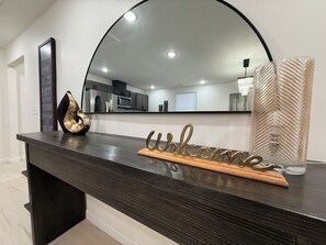 A dark wooden reception desk with a mirror above it, a 'Welcome' sign, and a decorative vase. - The 5th Street Retreat - Private Fenced Yard (Smithfield)
