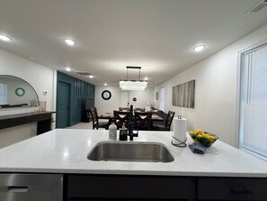 A modern kitchen with a central island, stainless steel sink, and a dining area with a chandelier. - The 5th Street Retreat - Private Fenced Yard (Smithfield)
