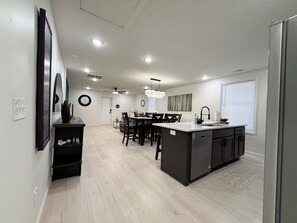 A modern kitchen with a central island, dining area with chairs, and a visible clock on the wall. - The 5th Street Retreat - Private Fenced Yard (Smithfield)