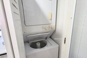 A compact, white laundry room with a built-in washer and dryer, a small window, and a door with a handle. - 2 BR Oceanfront OCNJ Condo - Beach Views & Dune Access! (Ocean City)