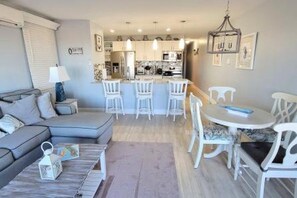 Ein modernes Wohnzimmer mit einem grauen Sofa, einem Couchtisch und einem Essbereich mit weißen Stühlen und einem kleinen Tisch.