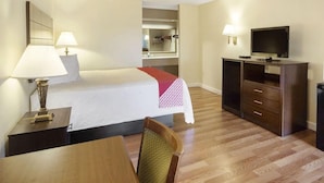 A hotel room with a bed, bedside table, lamp, TV, and a desk with a chair. - Days Inn & Suites by Wyndham Brewton (Brewton)