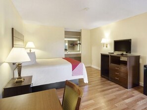 Habitación de hotel con cama, mesita de noche, lámpara, televisor y escritorio con silla.