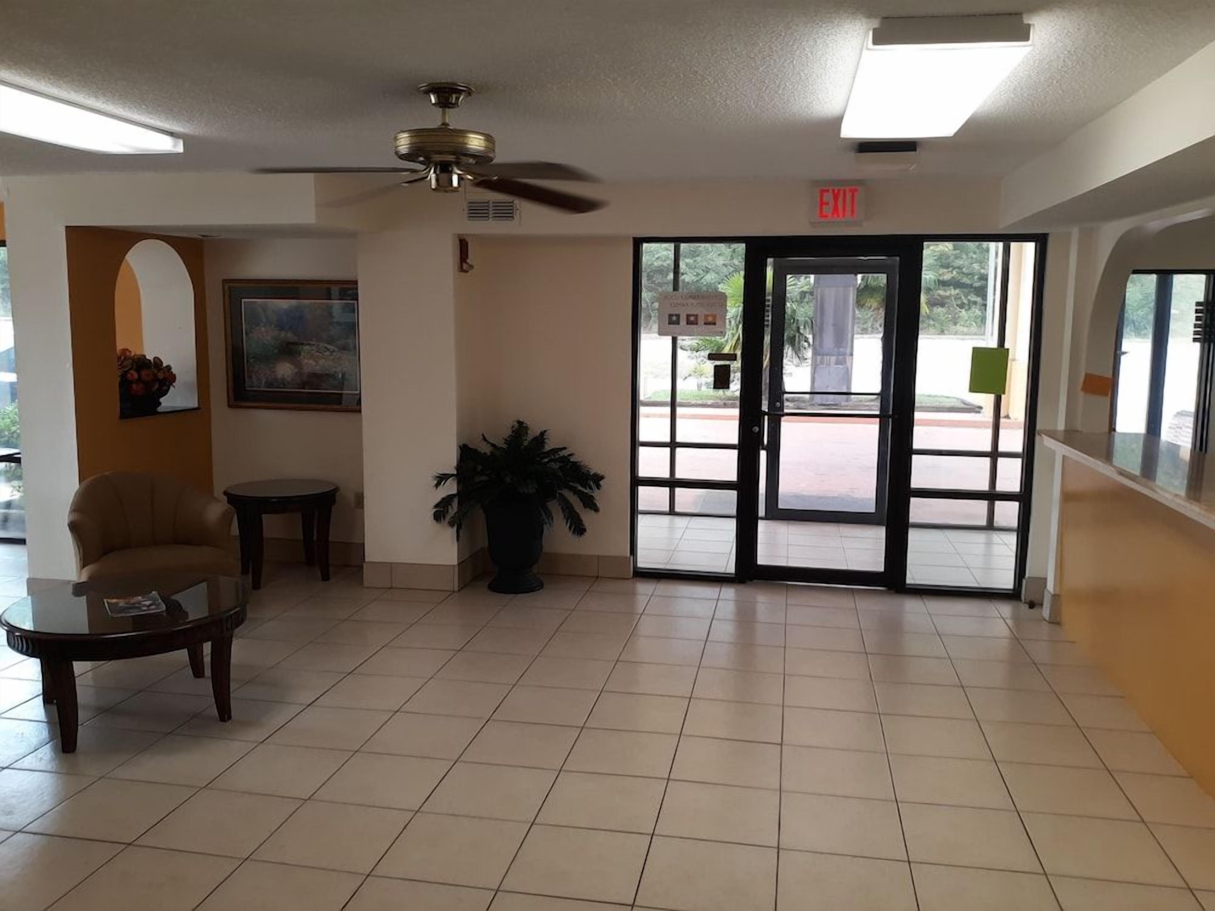 A lobby with a ceiling fan, a door marked 'EXIT,' a framed picture on the wall, and a potted plant.