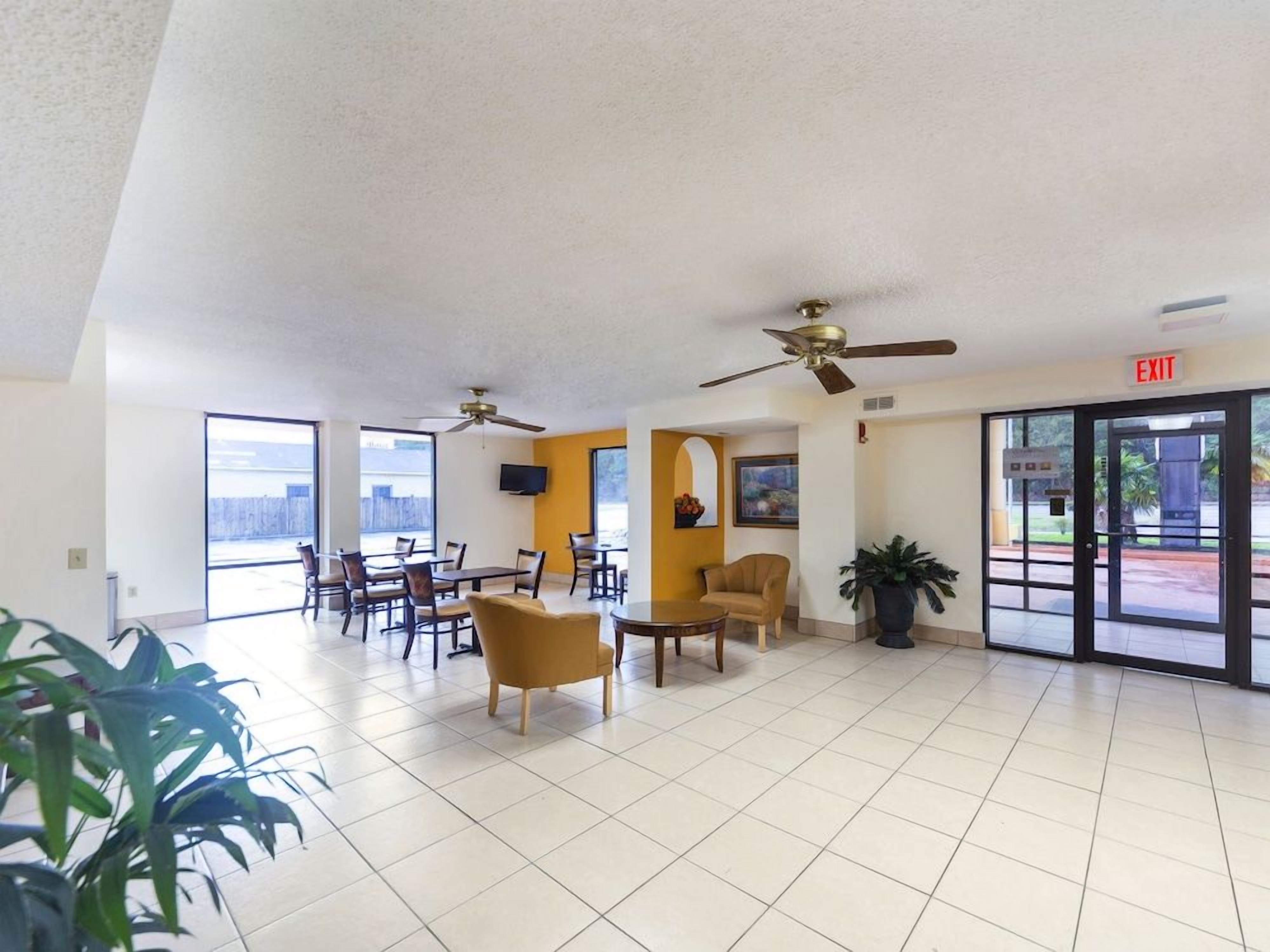 A spacious lobby with ceiling fans, a reception desk, and a view of the city through large windows.