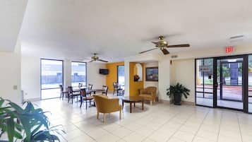 A spacious lobby with ceiling fans, a reception desk, and a view of the city through large windows.