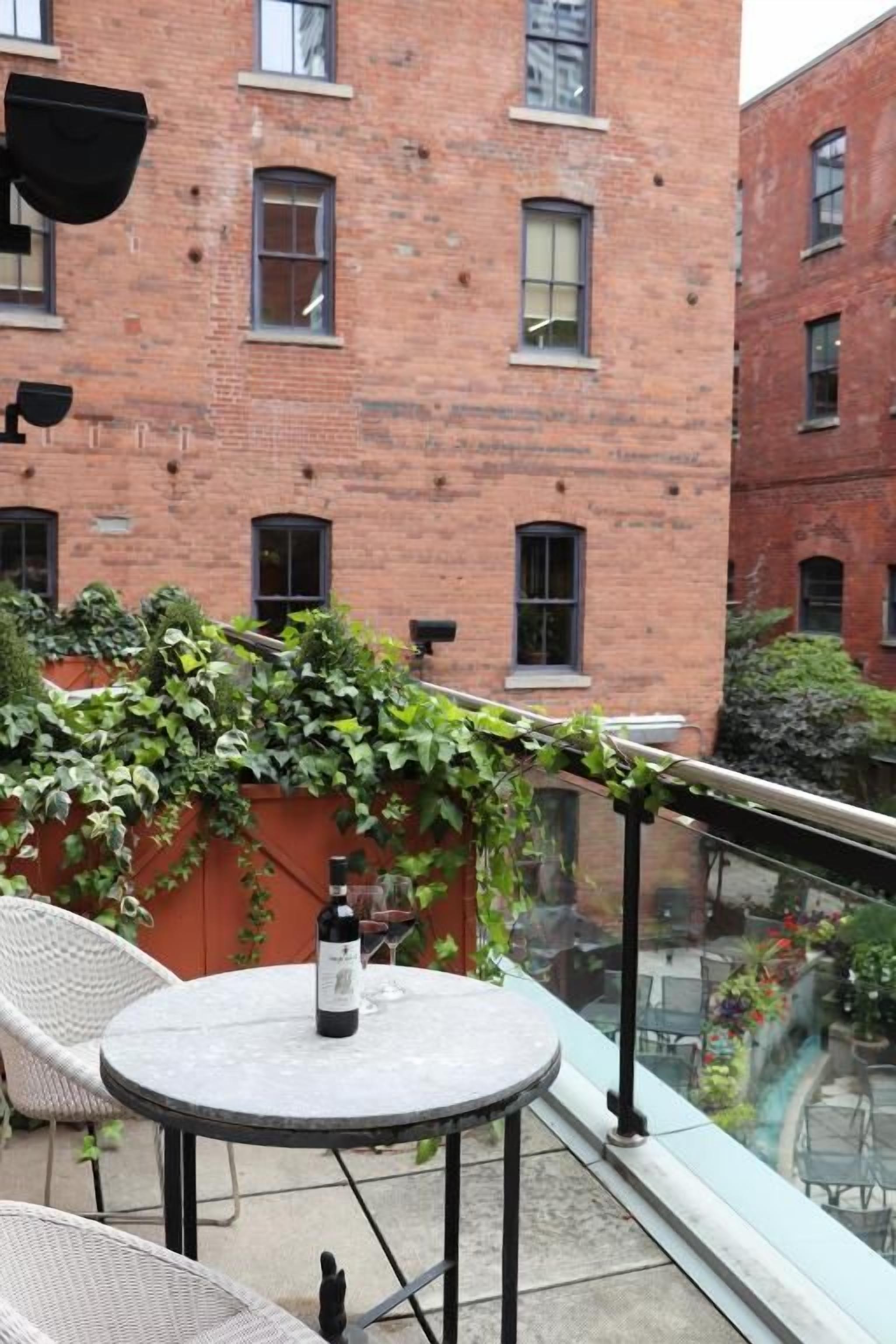 Una terraza en la azotea con una mesa, sillas, una botella de vino y vistas a un edificio de ladrillo.
