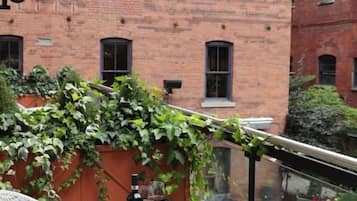 Una terraza en la azotea con una mesa, sillas, una botella de vino y vistas a un edificio de ladrillo.