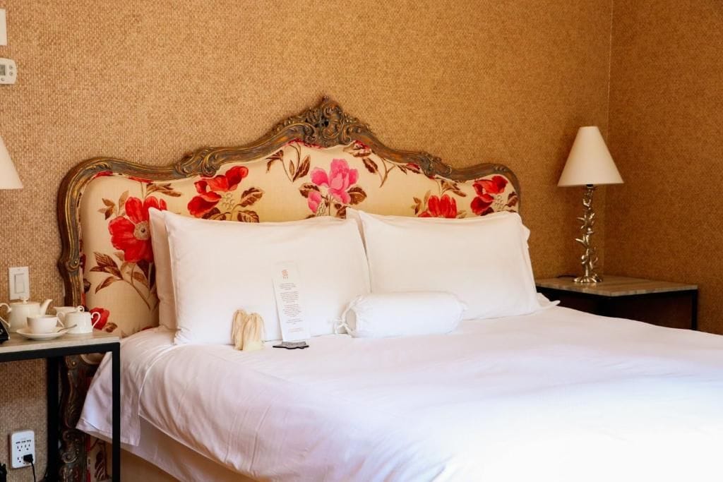 Habitación de hotel con cama, mesita de noche con lámpara y una pequeña mesa con tazas y teléfono.