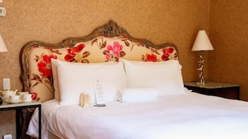 Habitación de hotel con cama, mesita de noche con lámpara y una pequeña mesa con tazas y teléfono.
