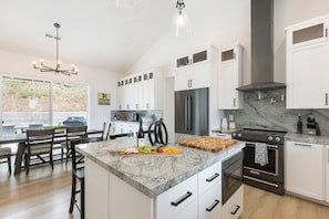 A modern kitchen with white cabinets, a marble countertop, a stainless steel refrigerator, and a black stove.